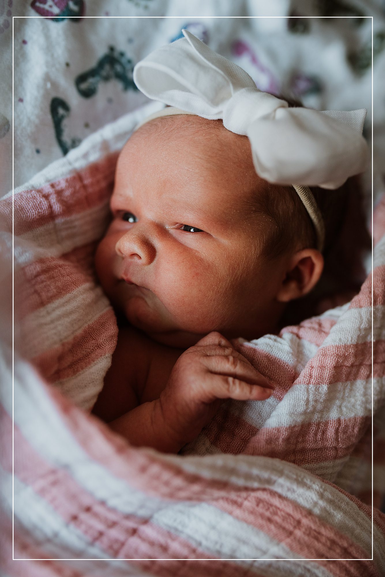 Close-up of a newborn baby wrapped in a soft pink and white swaddle, wearing a delicate white bow headband, captured in a peaceful Fresh 48 session in Utah.