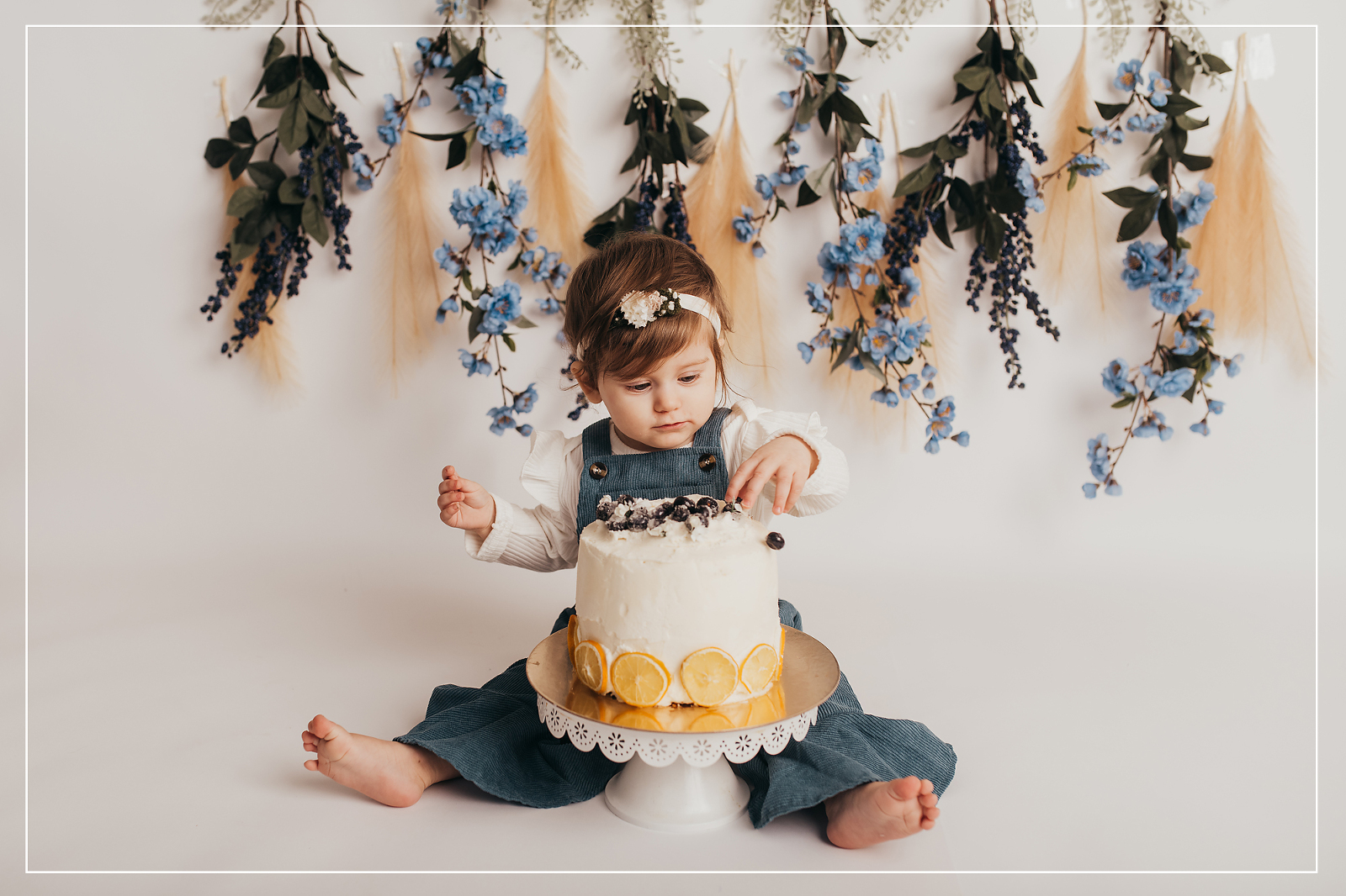 Adorable 1-year-old enjoying her first birthday smash cake session in Utah, surrounded by beautiful floral decor and a delicious cake.