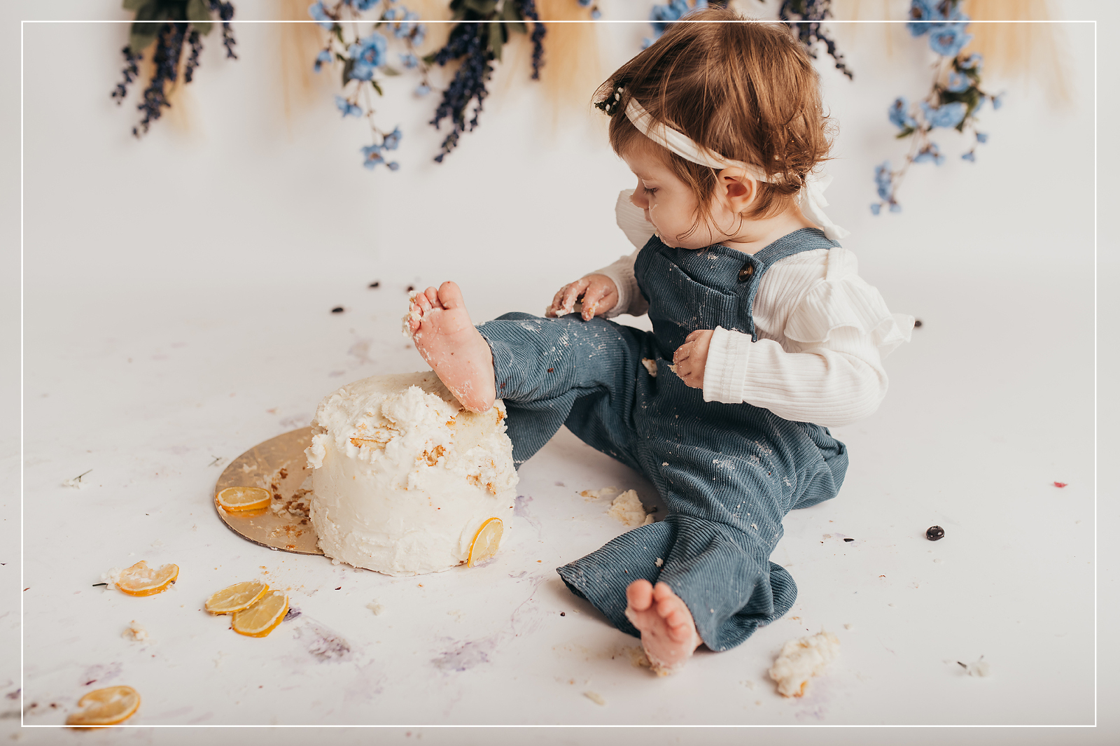 Adorable 1-year-old enjoying a messy and playful smash cake session in Utah, with cake on her foot and surrounding the cake stand.